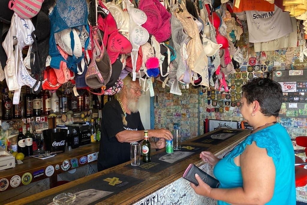 A lady purchasing drinks at a bar with bras hanging from the ceiling.