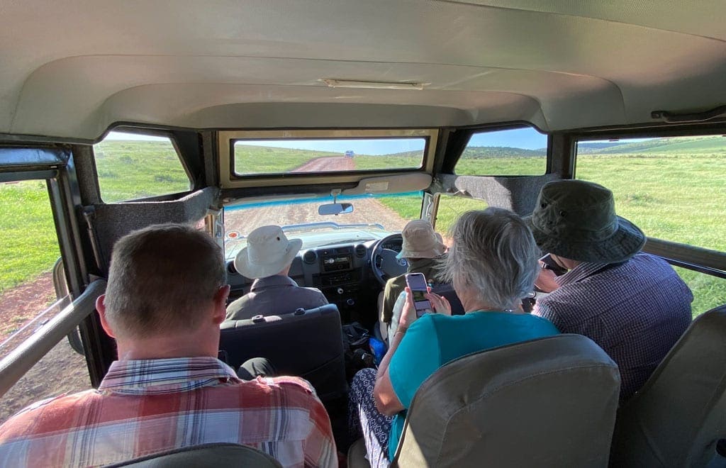The group sit inside the safari jeep as they travel along a road. 