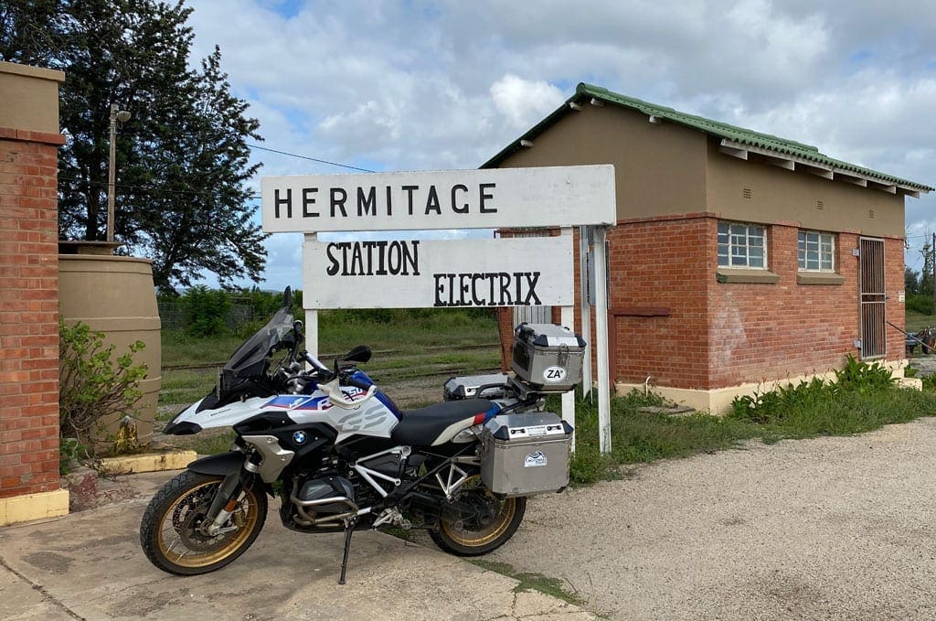 One of the bikes is parked outside a small building with a sign that says 'Hermitage, station electric'.
