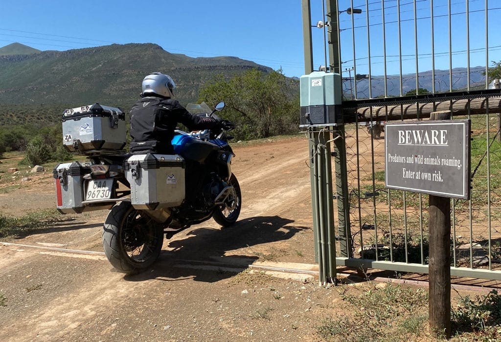 One of the bikers rides into a game reserve. A beware sign stand just outside the reserve's gate.