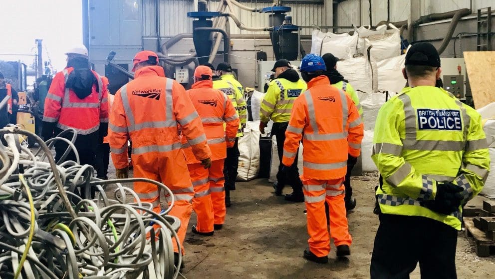 Members of Network Rail and BTP in visibility jackets stand inside a warehouse.