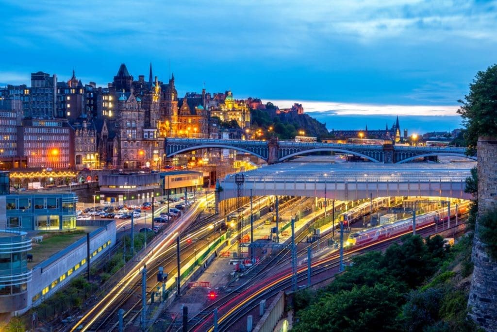 Edinburgh train station lit up by lights with the city in the background.