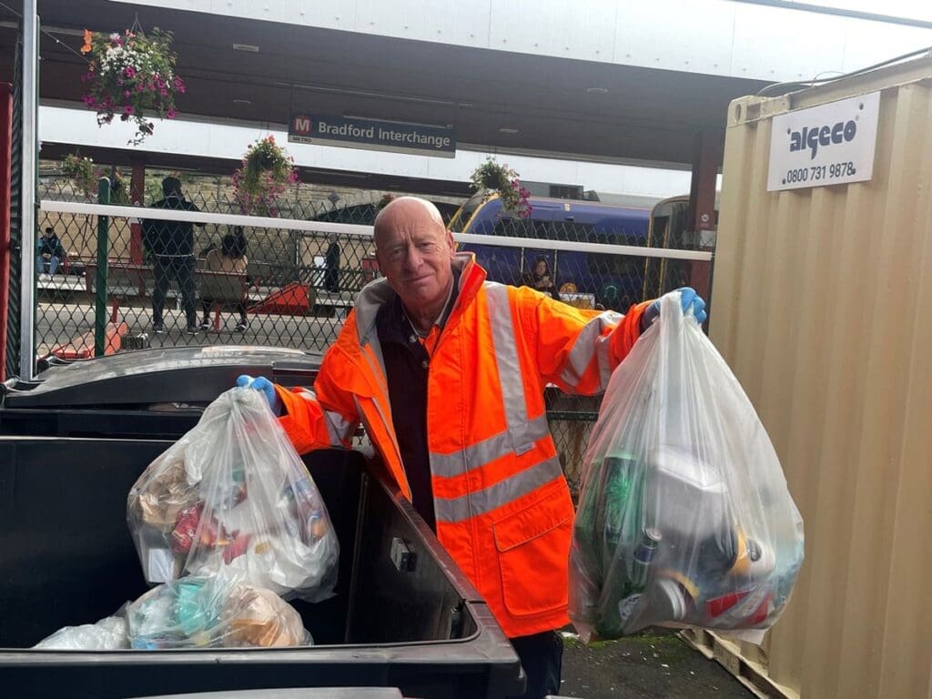 Dave Anderson at Bradford Interchange station, wearing high vis and holding two bin bags of rubbish and recycling