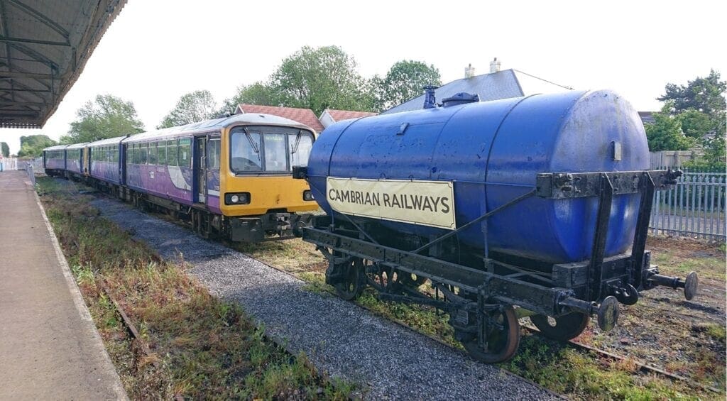 Class 144 Pacers Nos. 144006/07 are seen at their temporary new home after arrival on May 22– the CHR-owned former coal yard sidings a Gobowen. The restored tank promotes the Cambrian Heritage Railways project. PHIL BRADLEY/CHR