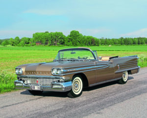 Shiny Oldsmobile parked on the road in front of fields