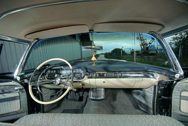 A photograph taken inside the Cadillac Sedan De Ville from the back seat, showing the wheel and dashboard.