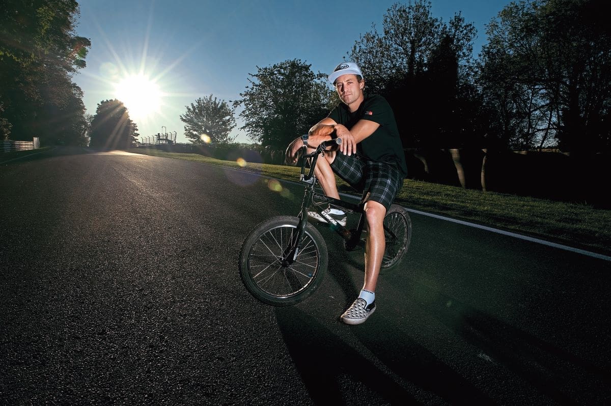 Josh Brookes on his bike in the middle of an empty road, the sun setting behind him.