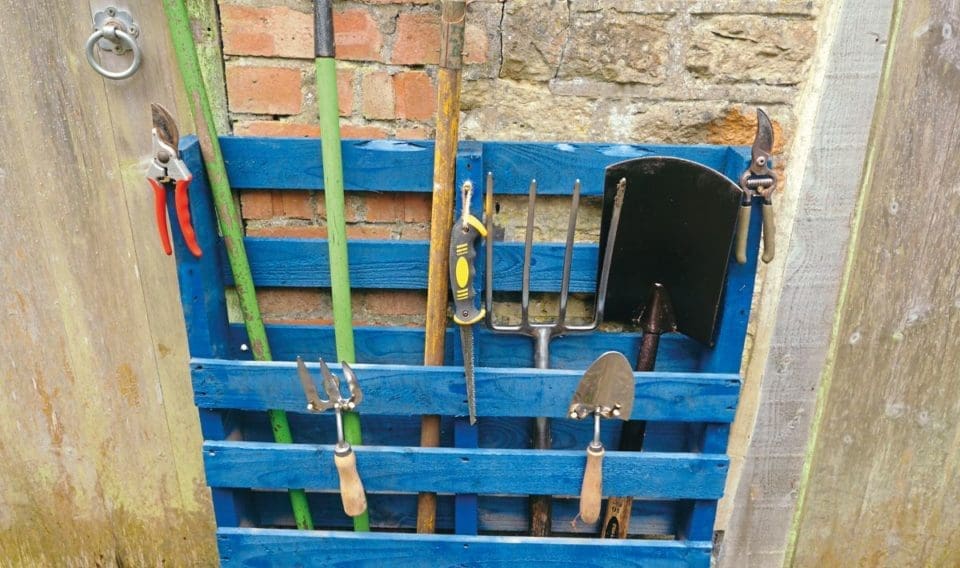 A blue wooden tool rack holding various garden tools.