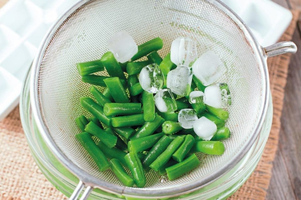 runner beans being blanched in a sieve with ice cubes
