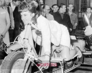 Black and white photo of a woman, Marlene Parker, on a scooter, with a crowd in the background