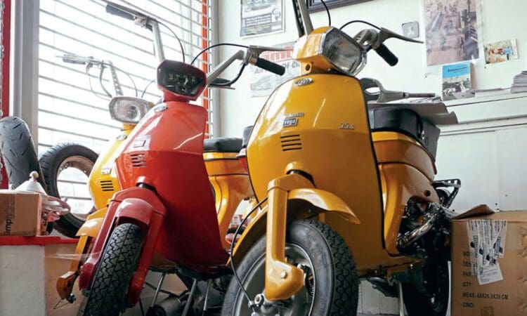 Three Luna scooters, 2 yellow and 1 red, in the front of the store by a window