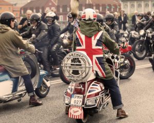 Mods wearing uk flag and rockers wearing leather clothes driving retro vespa scooters and mc at the Mods vs Rockers event