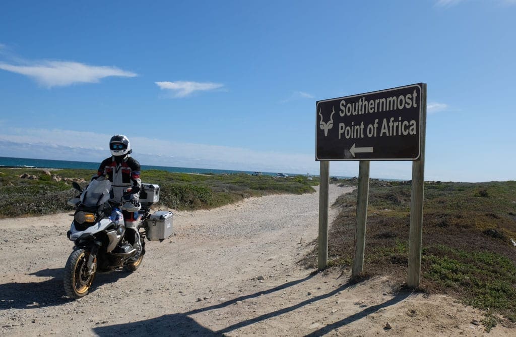 Tip of Africa 1 One of the bikers sits on their bike next to a sign saying 'Southernmost point of Africa'.