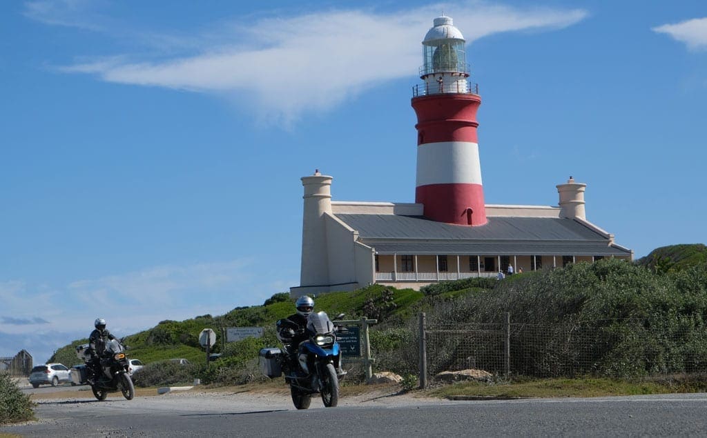 Two of the bikers ride past a lighthouse.
