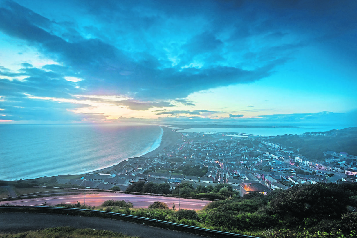 Beautiful dusk evening sky over Chesil Beach and the Jurassic Coast with tombolo connecting Fortuneswell to the mainland below and Weymouth in the distance, captured high up on the Isle of Portland, England