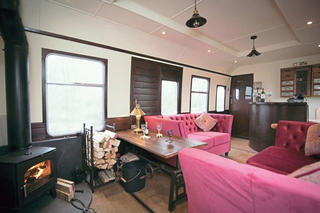 A view of the living room area with two coaches, table, wood-burning stove and bar.