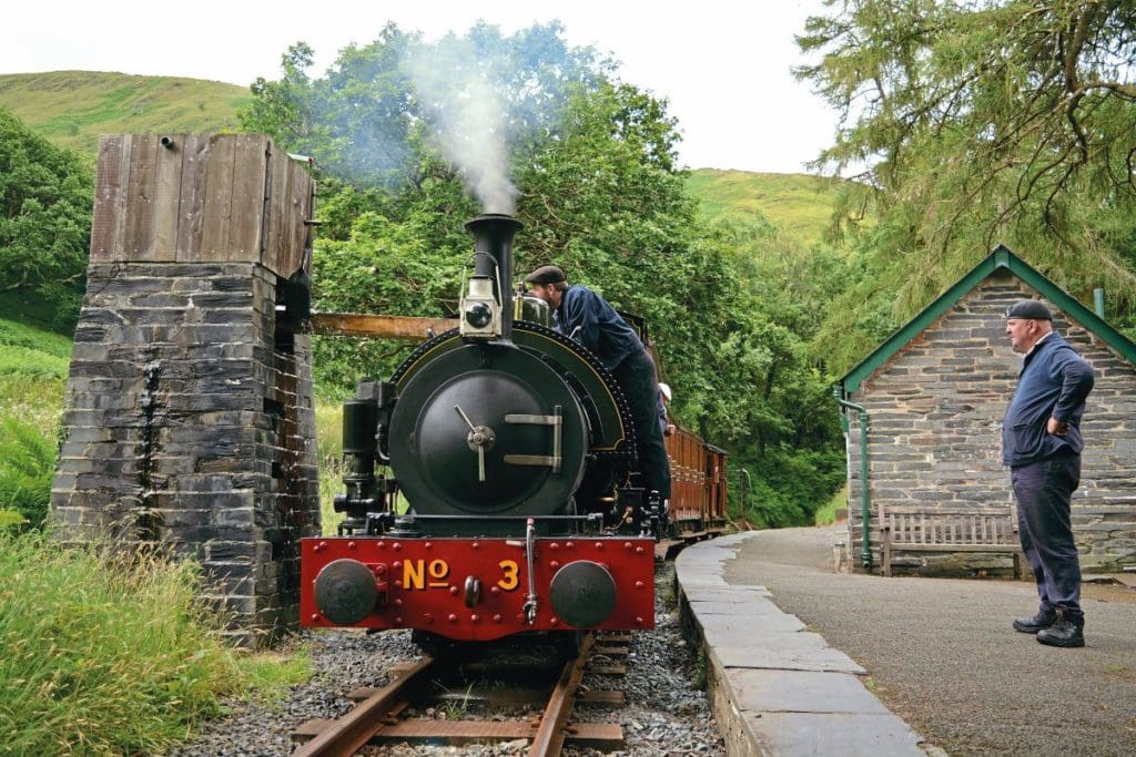 0-4-2ST No.3 Sir Haydn filling up at the original slate water column at Dolgoch station. Driver Chris Price, CEO of the North Yorkshire Moors Railway, watches on as cleaner Tom Allmark lines up the water trough. 