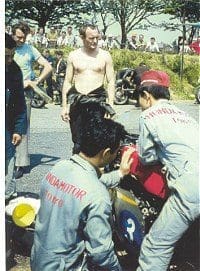 Mike Hailwood, looking pensive, as Honda technicians work on his 350cc six