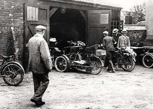 A Riley classic tricycle parked outside a garage door