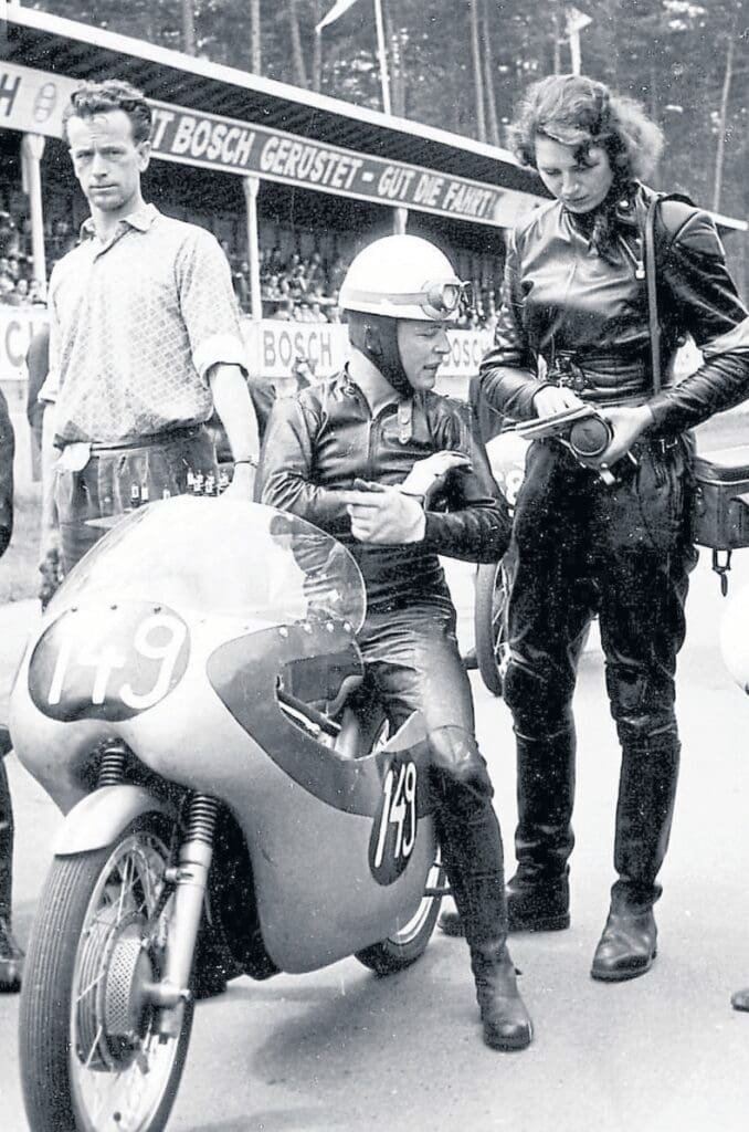 Camera and notepad in hand, interviewing Bultaco rider Ricardo Quintanilla at the German GP in 1961.