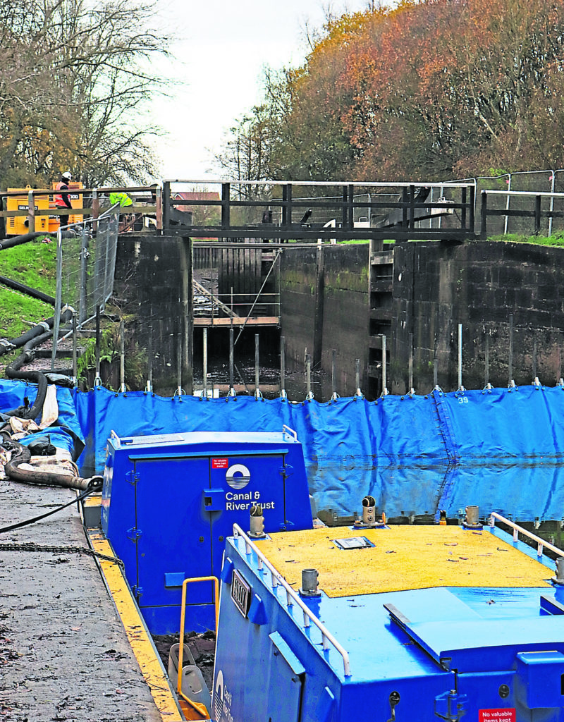 Removing the pipework from pumps that had been used to pump water around the Poolstock Lock No 2 while one of the Canal & River Trust workboats is moored on the lock landing and the fibre dam waits to be removed.