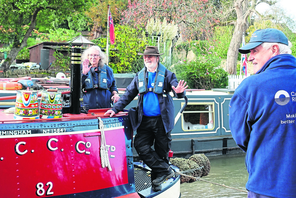 Making waves. Kathryn Doddington and Rob Westlake acknowledge people on the canalside as Sculptor is at last tied up back at Stoke Bruerne, almost a year after heading north for major repairs.