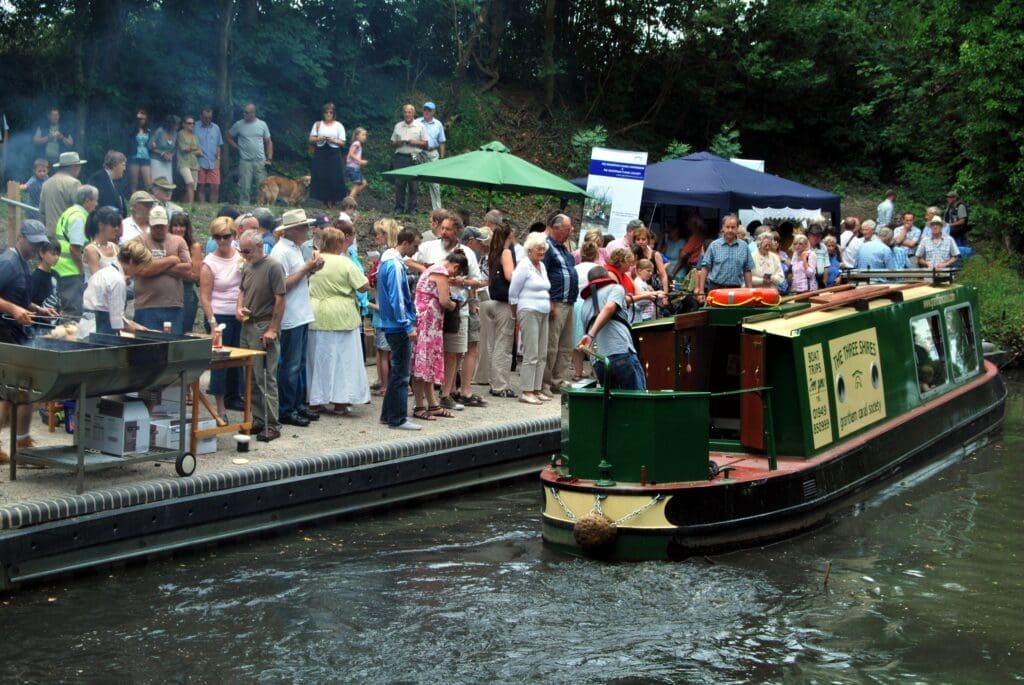 A busy Harlaxton Wharf, on the Grantham Canal, on the day it was officially opened following restoration in 2009. It is a mooring for the society’s trips on Three Shires; visit https://granthamcanal.org/boat-trips-cruises/ RUSS HAMER – CC BY-SA 3.0